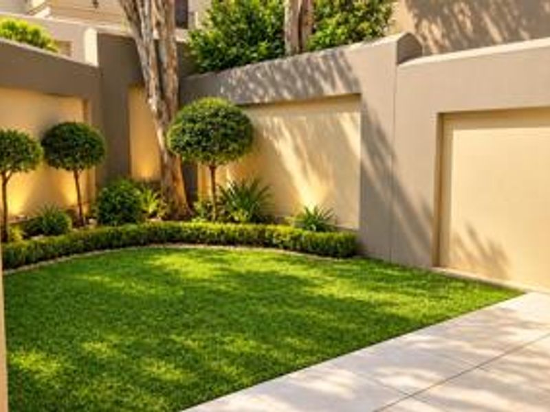 A well-maintained private garden area featuring manicured lawn, structured topiary, boundary walls, and integrated landscape lighting.