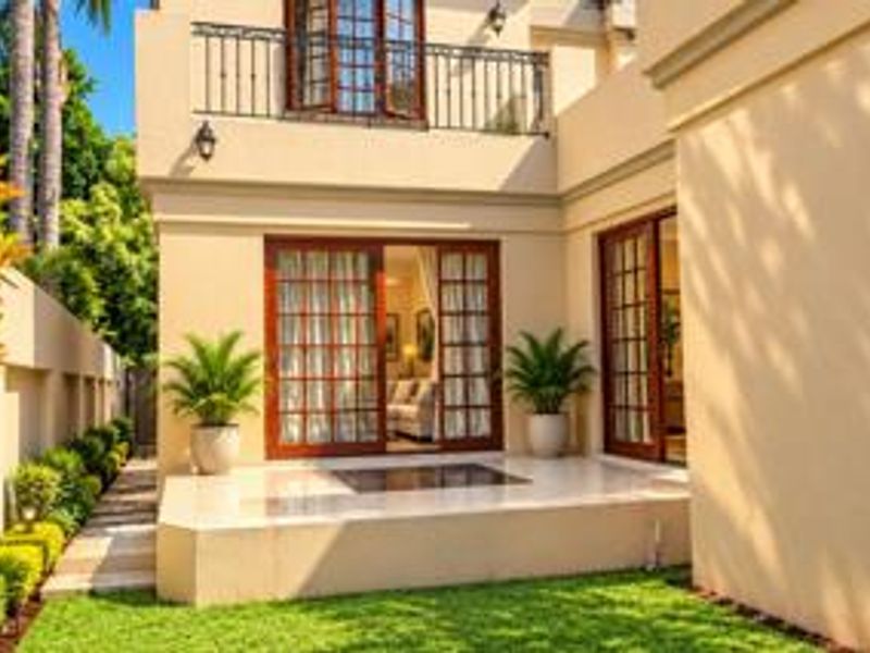 A well-maintained rear exterior featuring a stone patio, sliding glass doors, and an upper-level balcony with wrought iron railings.