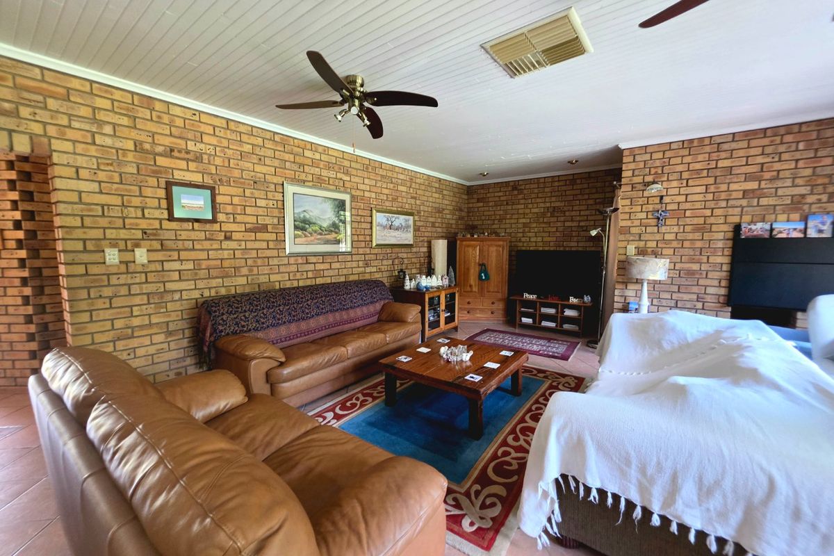 Spacious living room featuring exposed brick walls, tiled flooring, and a ceiling fan, offering a warm and traditional aesthetic.