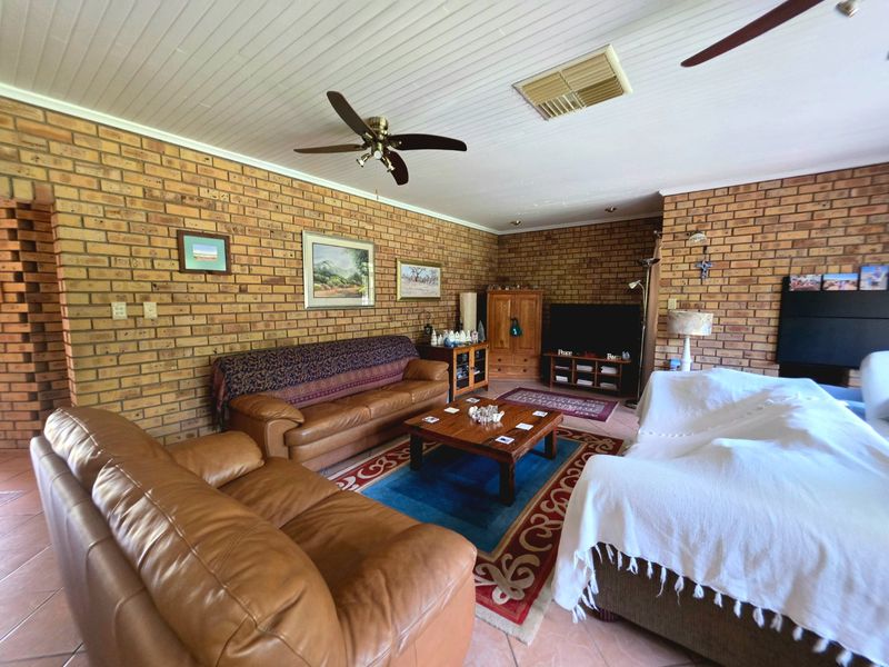 Spacious living room featuring exposed brick walls, tiled flooring, and a ceiling fan, offering a warm and traditional aesthetic.
