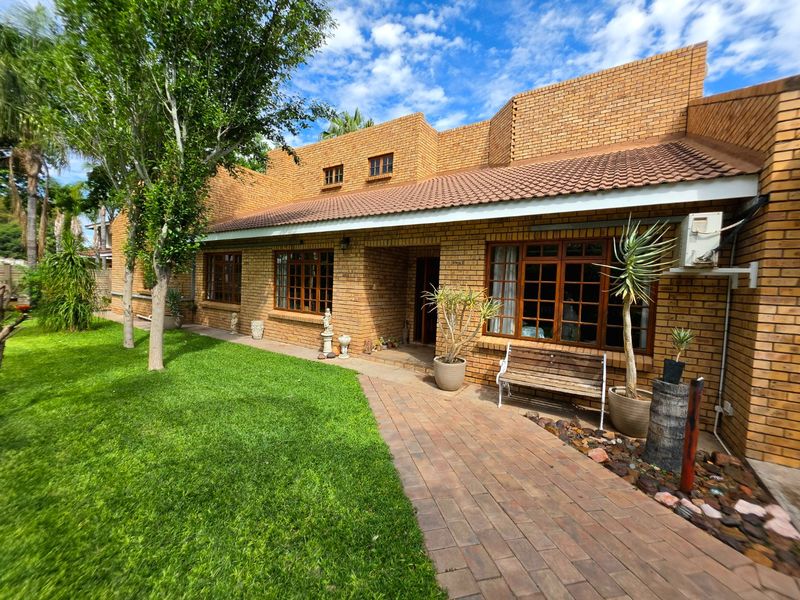 A well-maintained face brick house exterior featuring a tiled roof, timber frame windows, and a paved walkway leading to the entrance.