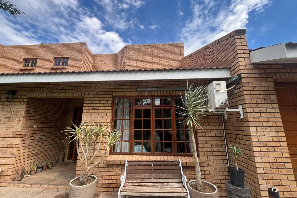 A rear exterior view of a face brick house featuring timber frame windows, a covered patio area, and an external air conditioning unit.