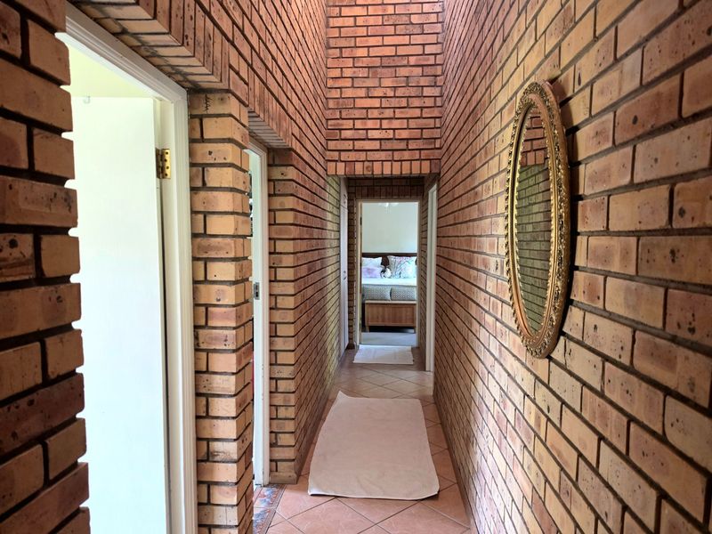 A long hallway featuring exposed brick walls and tiled flooring, providing access to multiple rooms within the home.