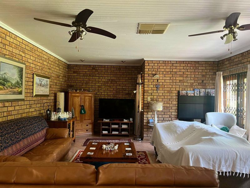 Spacious living room featuring exposed brick walls, tiled flooring, and dual ceiling fans, with direct access to the exterior through a sliding glass door.