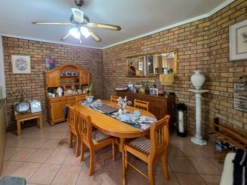 Dining room featuring exposed brick walls, tiled flooring, and a ceiling fan, offering a rustic aesthetic with potential for modern updates.