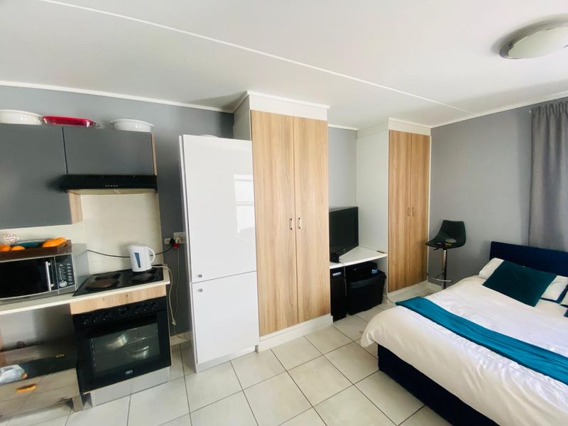Compact open-plan studio featuring a functional kitchenette with built-in cabinetry, electric oven, hob, and tiled flooring throughout.