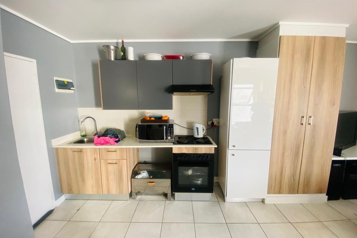 Compact kitchen featuring modern wood-look cabinetry, tiled flooring, built-in oven with hob, and an integrated extractor fan.