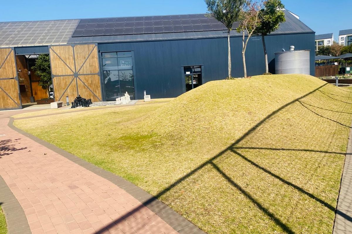 A well-maintained rear exterior area featuring a modern building with solar panels, a water tank, and a landscaped grass mound alongside a paved walkway.