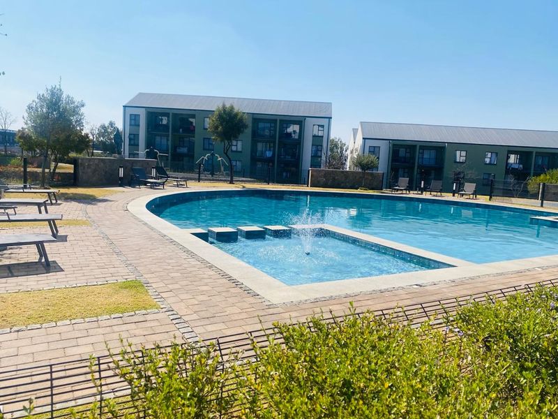 A well-maintained communal swimming pool area featuring a water fountain, paved decking, and landscaped surroundings within a residential complex.