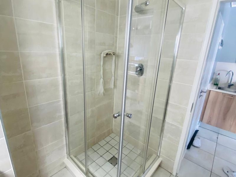 A functional bathroom featuring a corner shower enclosure with glass doors, tiled walls and flooring, and an adjacent vanity basin area.