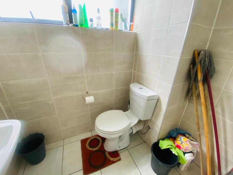A functional bathroom featuring neutral ceramic wall and floor tiling, equipped with a standard toilet and window for natural light.