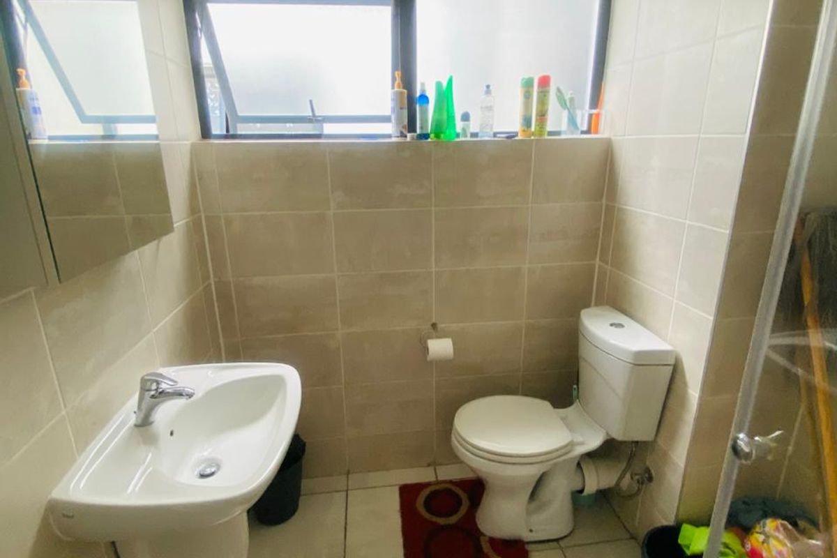 A functional bathroom featuring tiled walls and flooring, a wall-mounted basin, a toilet, and a glass-enclosed shower area.
