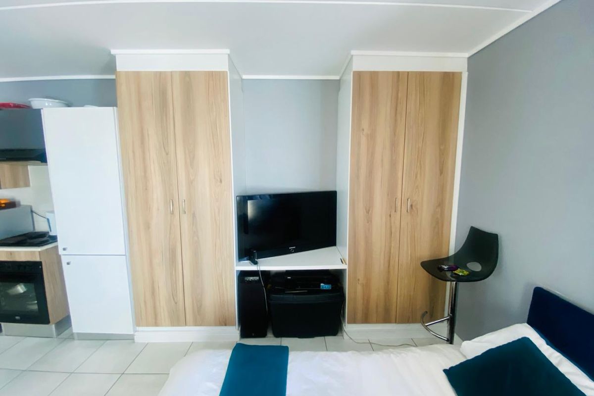 A bedroom featuring light wood-finish built-in cupboards with integrated shelving and tiled flooring.
