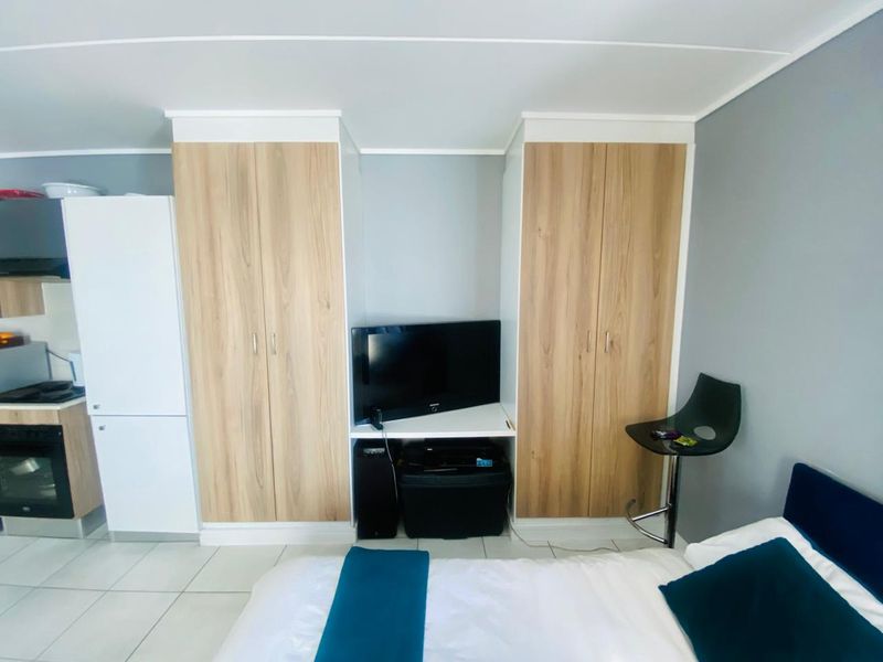 A bedroom featuring light wood-finish built-in cupboards with integrated shelving and tiled flooring.