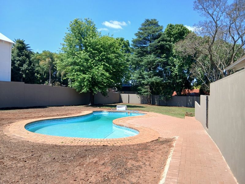 A private backyard featuring a kidney-shaped swimming pool surrounded by brick paving and a perimeter wall, with surrounding garden space currently undergoing landscaping.