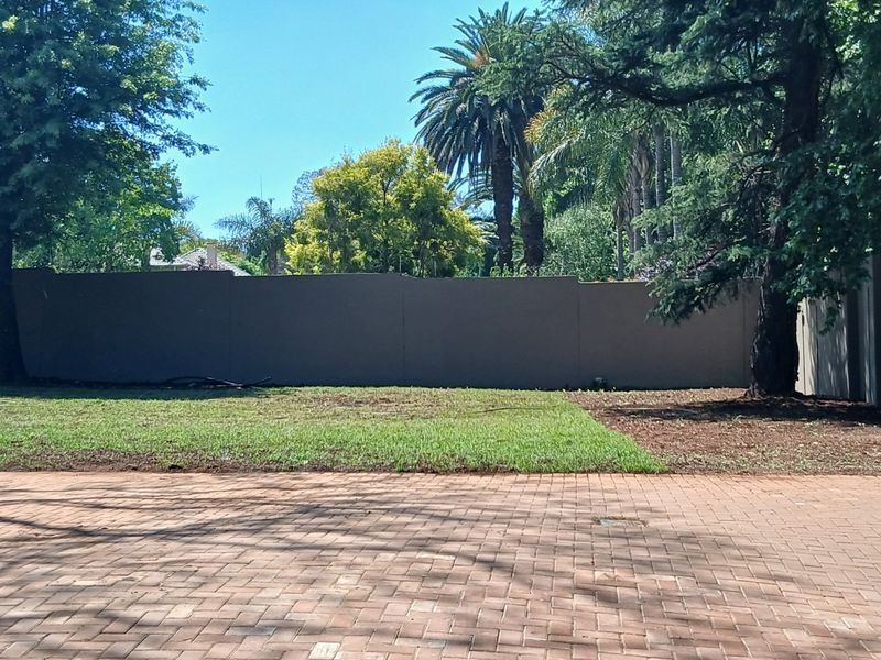A private rear garden featuring a paved patio area, established lawn, and a solid boundary wall surrounded by mature trees.