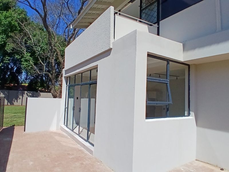 Rear view of the townhouse featuring a paved patio area, a balcony above, and modern metal-framed windows and sliding doors.