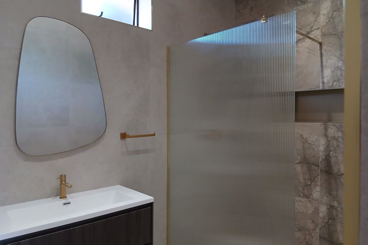 Modern bathroom featuring a vanity with brass faucet, fluted glass shower screen, and elegant marble-look wall tiles with a recessed shower niche.