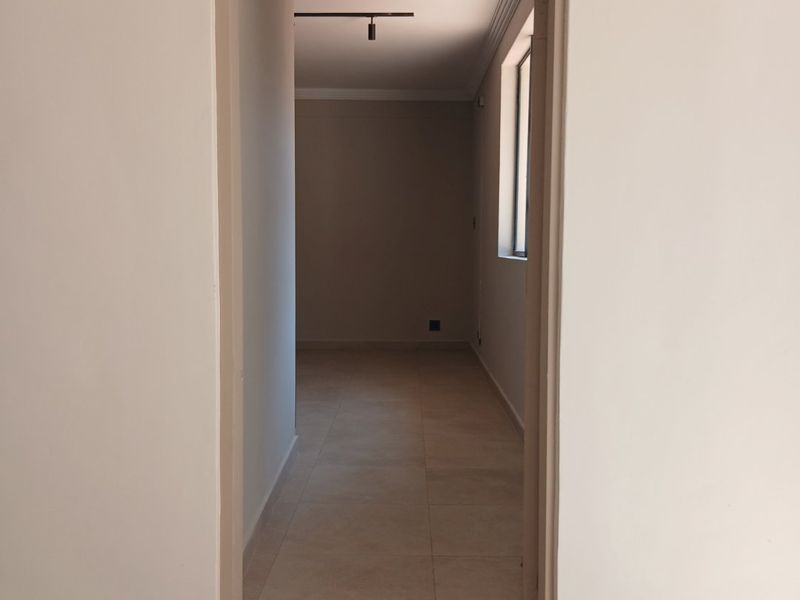 A clean, empty hallway featuring neutral tiled flooring, modern track lighting, and decorative cornicing, leading into an adjacent room.