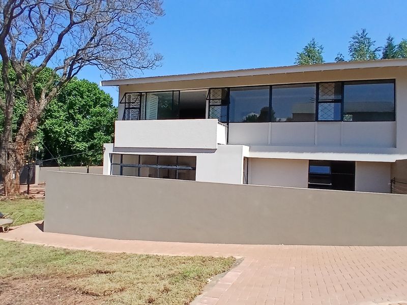Rear view of the townhouse featuring a balcony, large windows, a paved driveway, and a surrounding boundary wall.