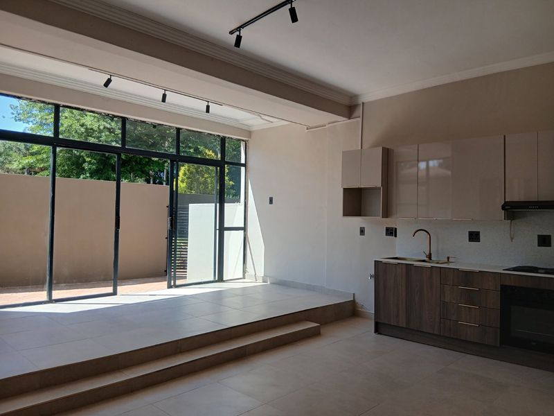 Modern open-plan living area featuring a sleek kitchen with built-in appliances, tiled floors, and large sliding doors opening to an outdoor patio space.