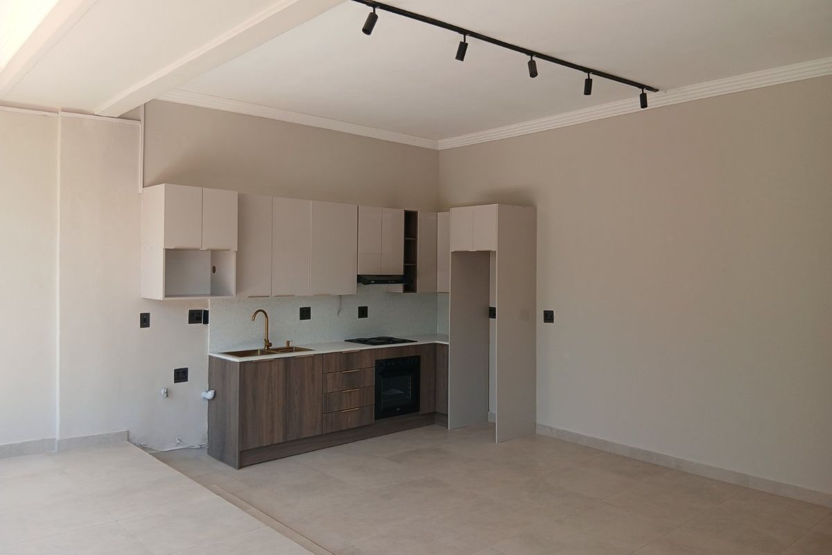 Modern open-plan kitchen featuring sleek cabinetry, integrated oven, hob, extractor fan, and contemporary track lighting in a neutral, well-maintained space.