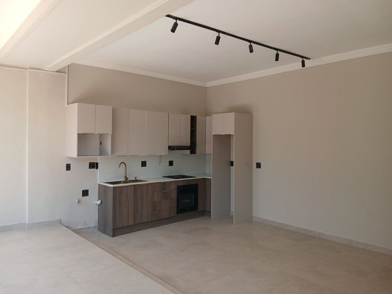 Modern open-plan kitchen featuring sleek cabinetry, integrated oven, hob, extractor fan, and contemporary track lighting in a neutral, well-maintained space.