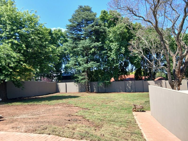A spacious private garden area featuring a perimeter boundary wall, mature trees, and a paved walkway, offering potential for landscaping and outdoor development.