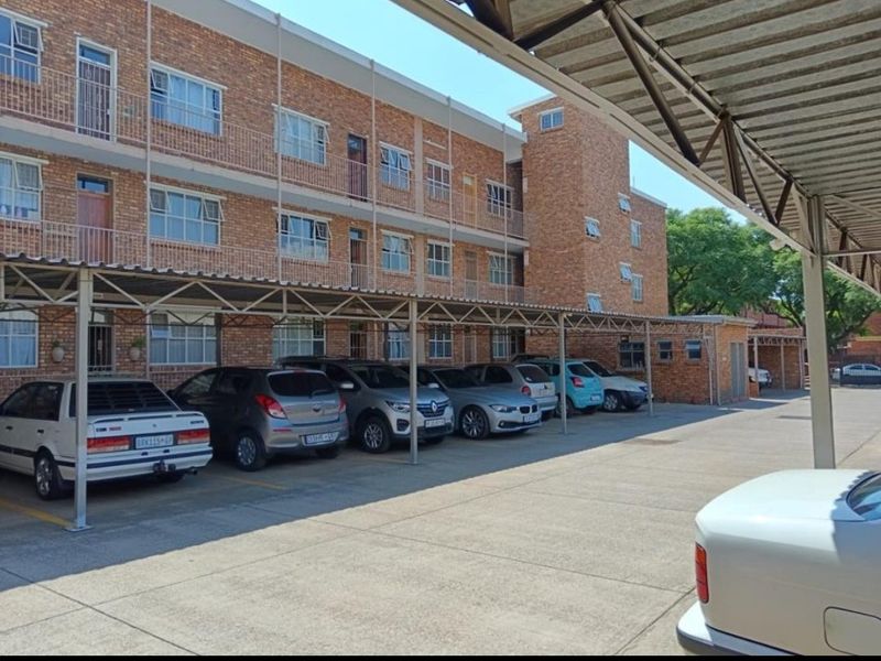 Exterior view of a multi-story brick apartment building featuring covered parking bays and concrete driveway access.
