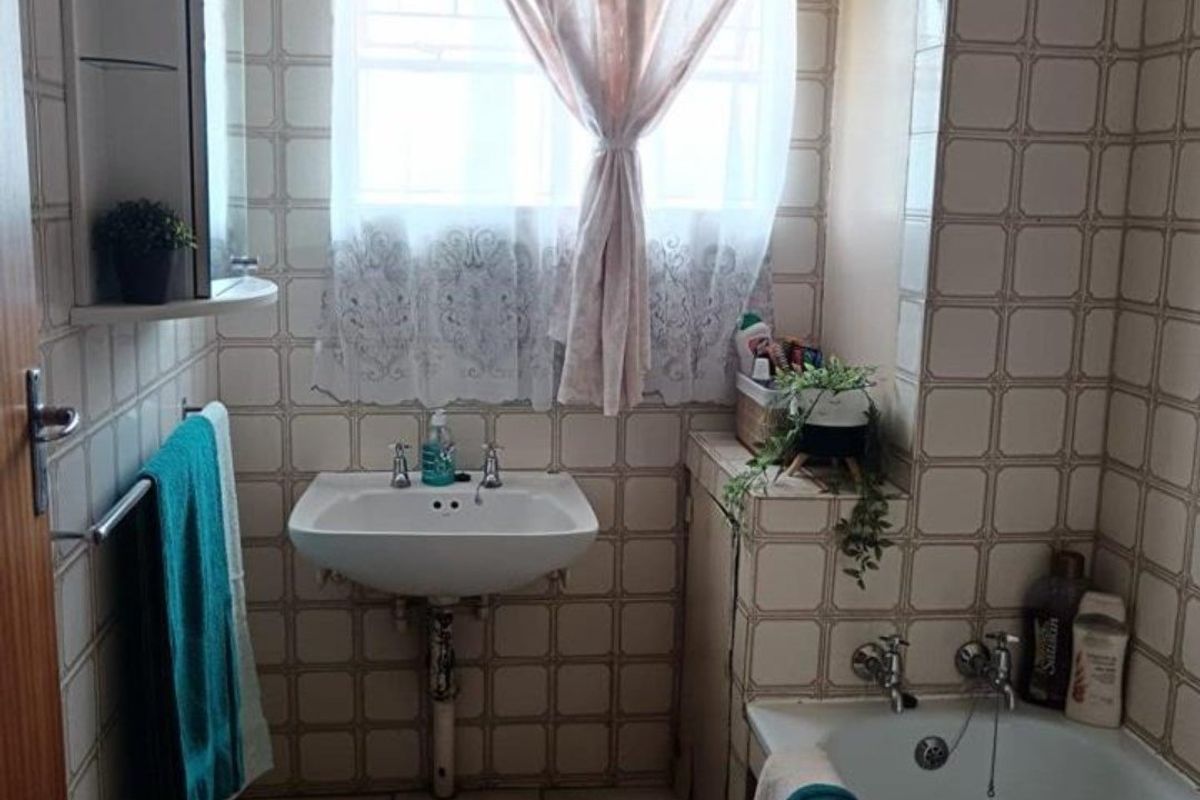A compact bathroom featuring a wall-mounted basin, built-in bathtub, and full-height ceramic wall tiling. The space offers a functional layout with classic finishes.