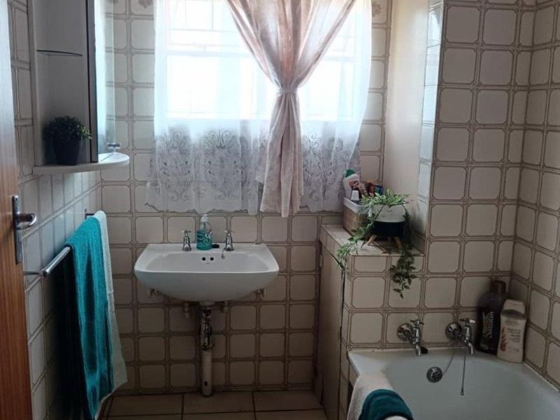 A compact bathroom featuring a wall-mounted basin, built-in bathtub, and full-height ceramic wall tiling. The space offers a functional layout with classic finishes.