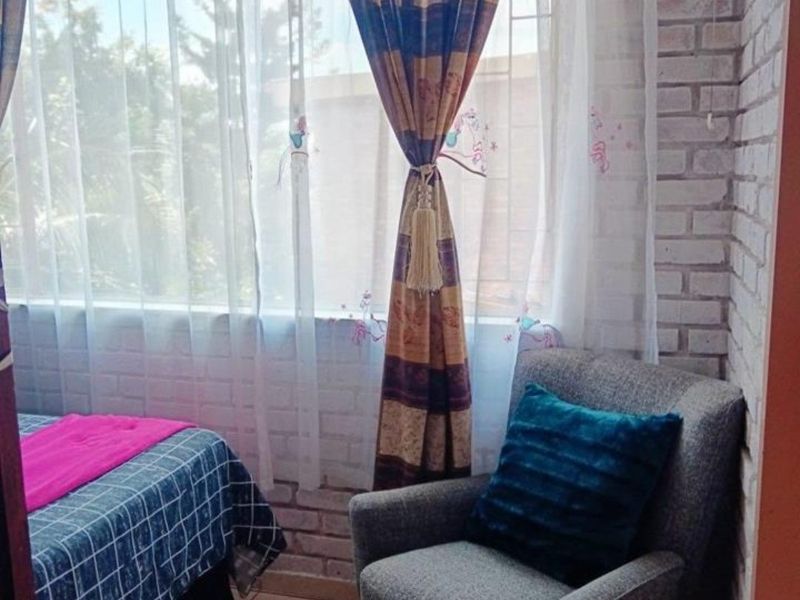 A cozy bedroom featuring an exposed brick accent wall, tiled flooring, and a large window with security bars.