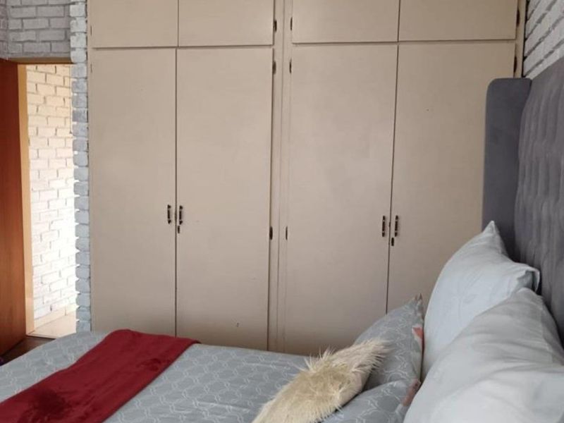 A bedroom featuring floor-to-ceiling built-in cupboards and a textured exposed brick wall finish.