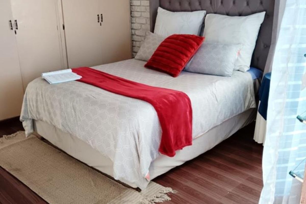 A cozy bedroom featuring laminate flooring, a textured exposed brick feature wall, and ample built-in cupboard storage.