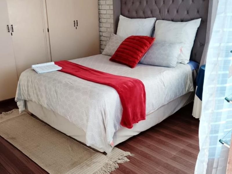 A cozy bedroom featuring laminate flooring, a textured exposed brick feature wall, and ample built-in cupboard storage.