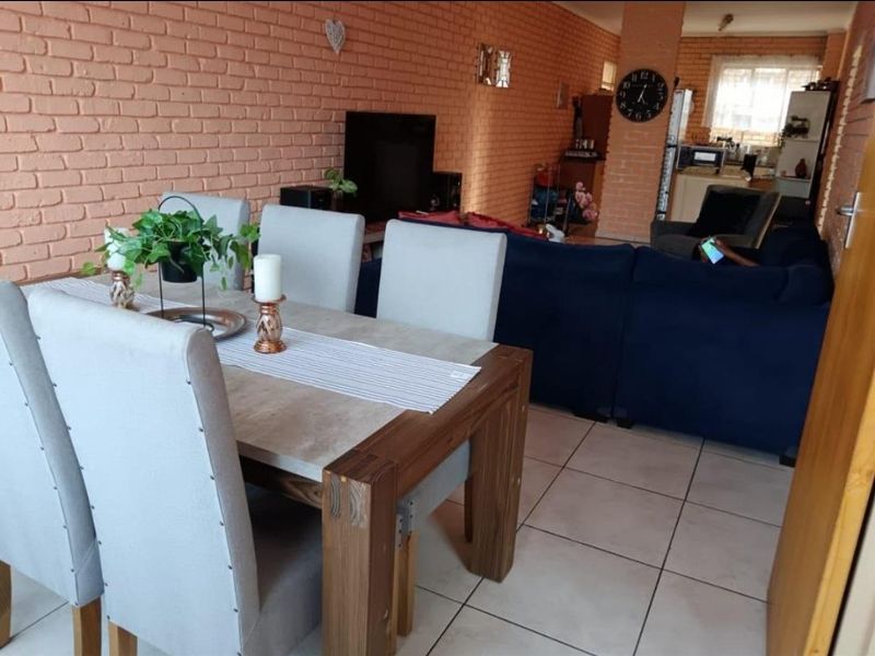 Open-plan living and dining area featuring exposed brick walls and neutral ceramic floor tiles, creating a connected and functional living space.