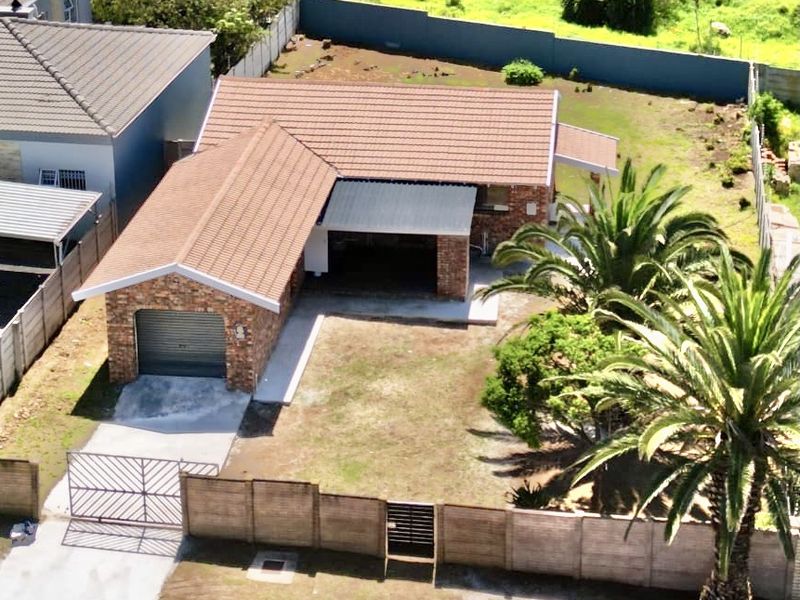 Aerial view of a single-story brick house featuring a tiled roof, attached garage, perimeter wall, and established garden with palm trees.