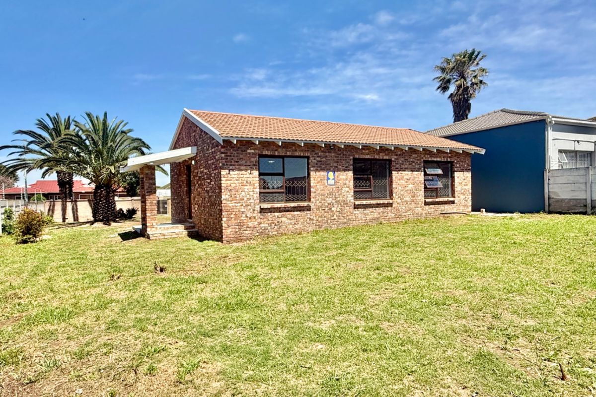 A detached face brick house featuring a tiled roof and aluminium window frames, set on a spacious grassed plot.