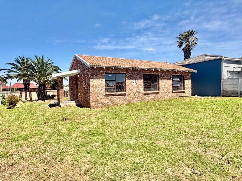 A detached face brick house featuring a tiled roof and aluminium window frames, set on a spacious grassed plot.