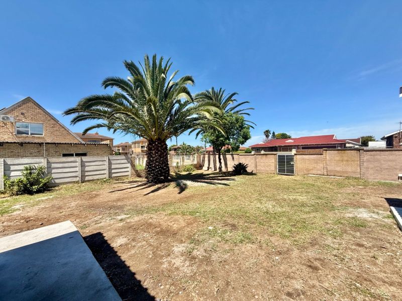 A spacious backyard featuring a large palm tree, concrete patio area, and perimeter boundary walls, offering potential for landscaping and outdoor improvement.