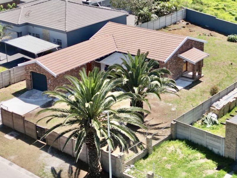 Aerial view of a single-story brick house featuring a tiled roof, concrete driveway, and a large garden area enclosed by perimeter walls.
