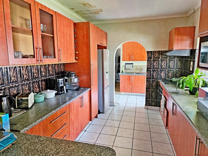 A functional kitchen featuring laminate cabinetry, granite countertops, and a tiled backsplash, with an adjacent scullery area accessible through an arched doorway.