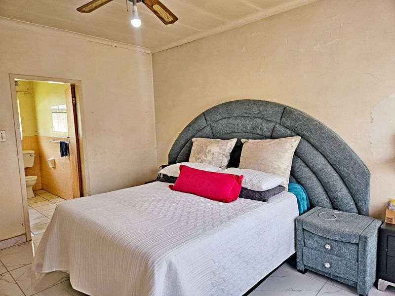 A bedroom featuring tiled flooring and a ceiling fan, with visible wear to the wall finishes requiring maintenance or cosmetic updates.