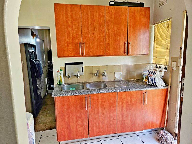 A functional scullery area featuring laminate cabinetry, a stainless steel double sink, granite-look countertops, and tiled flooring.
