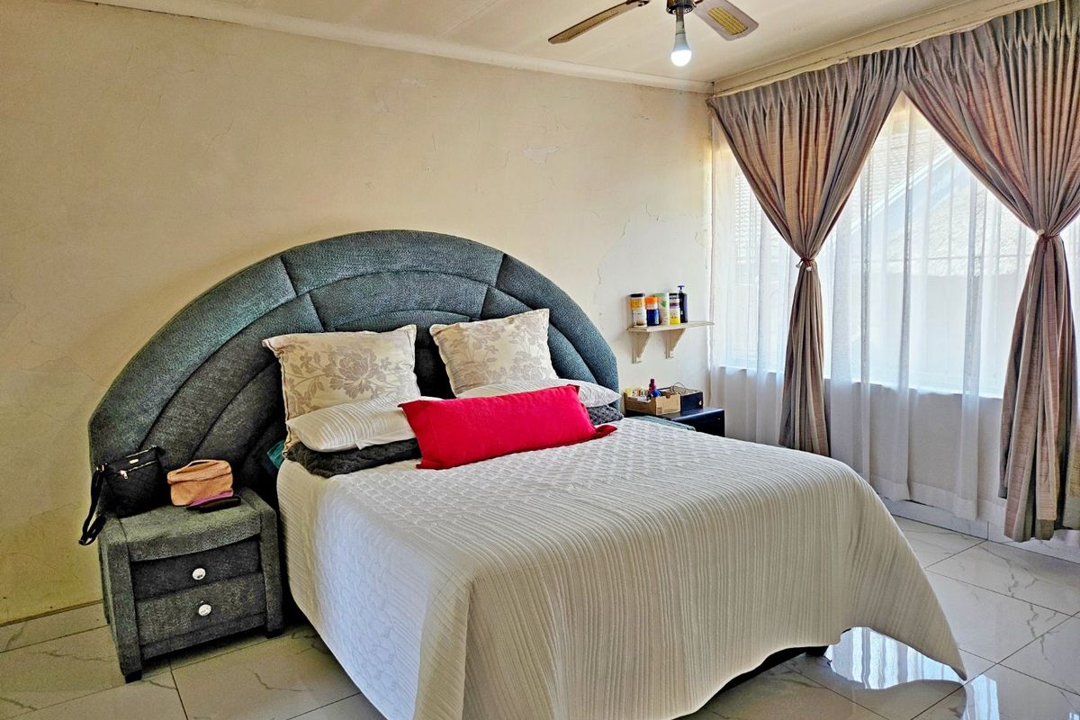 A bedroom featuring tiled flooring and a ceiling fan, currently showing signs of wear on the walls requiring maintenance and cosmetic updates.