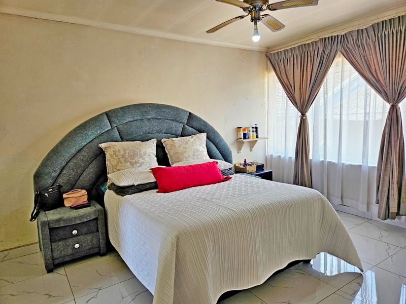 A bedroom featuring tiled flooring and a ceiling fan, currently showing signs of wear on the walls requiring maintenance and cosmetic updates.