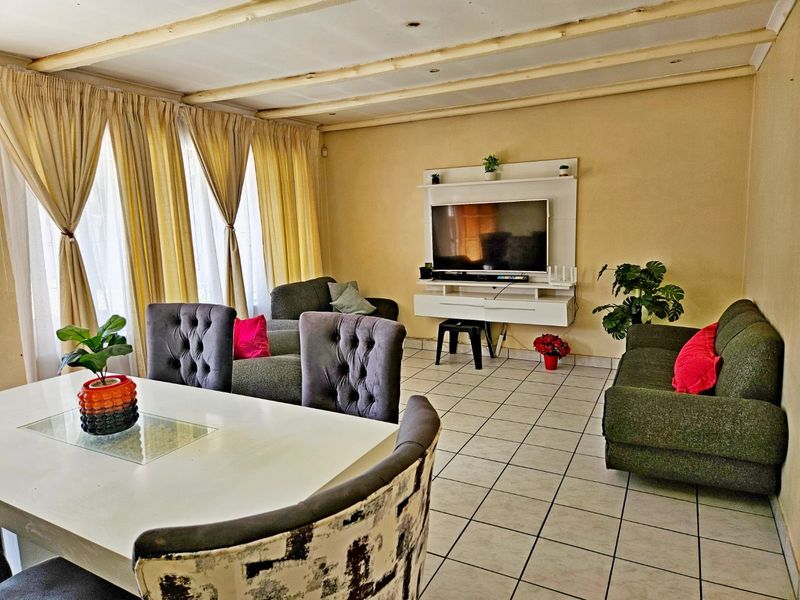 Open-plan living and dining area featuring tiled flooring, exposed beam ceiling, and a built-in media console unit.