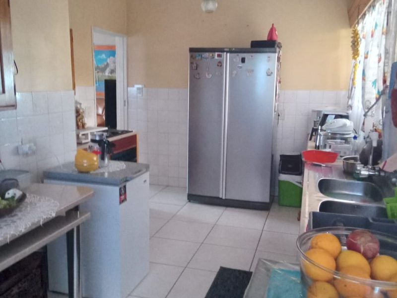 A functional kitchen featuring tiled flooring, a double stainless steel sink, and a tiled splashback, offering a practical layout for daily meal preparation.