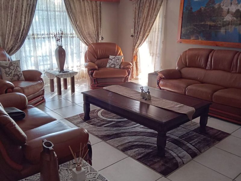 A spacious living room featuring tiled flooring, a ceiling fan, and decorative curtain pelmets, offering a comfortable and functional family living space.