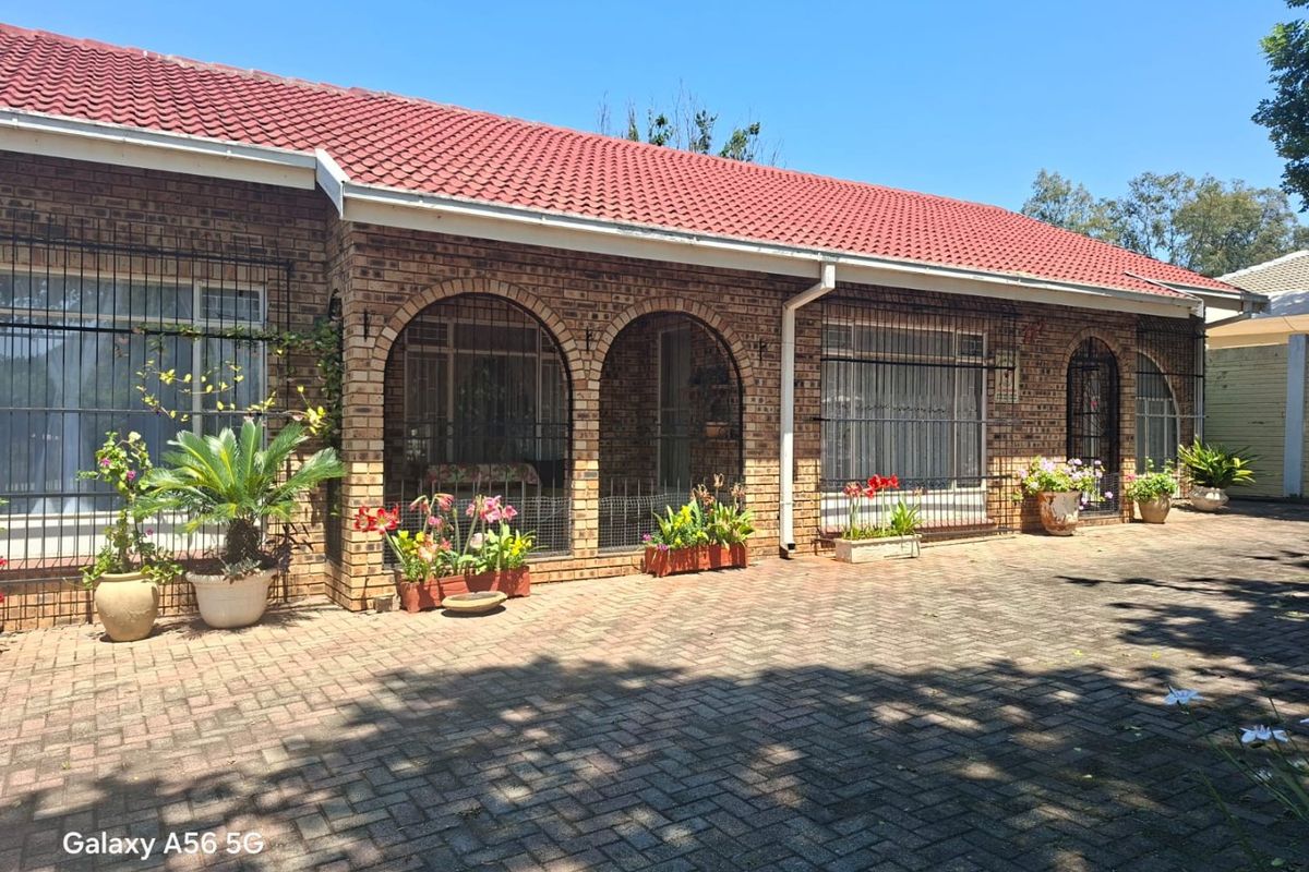 Rear view of a face brick house featuring an arched patio area and paved outdoor space under a tiled roof.